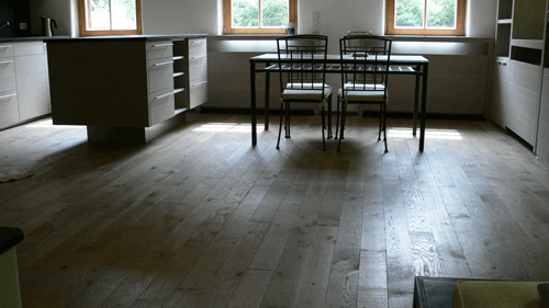 Küche mit Holzboden, Tisch und Stühlen, große Fenster mit natürlichem Licht.