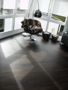 Moderne Wohnung mit dunklem Holzboden, einem eleganten Sessel und einer Pendelleuchte.