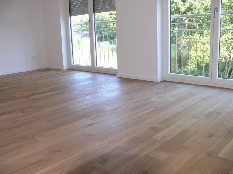 Heller Raum mit Holzboden und großen Fenstern, die auf einen Balkon führen.