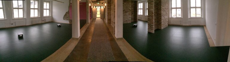 Panoramablick auf einen langen, hell erleuchteten Gang mit fensterlosen Wänden.