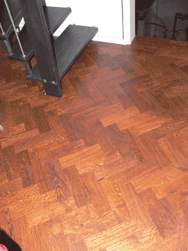 Dunkles Parkettboden mit einer Treppe im Hintergrund.