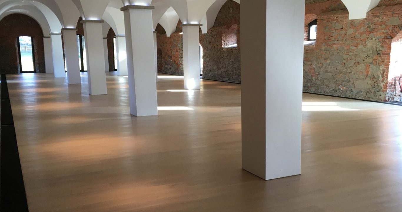 Bodenleger Service Heller, offener Raum mit Holzfußboden und säulengegliedertem Deckenbereich.