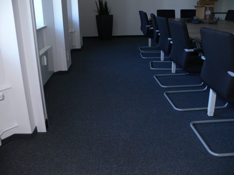 Büro mit Teppichboden und schwarzen Stühlen um einen Konferenztisch.