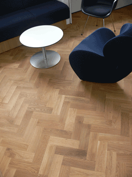 Holzboden im Fischgrät-Muster, blaue Polstermöbel und runder Tisch.